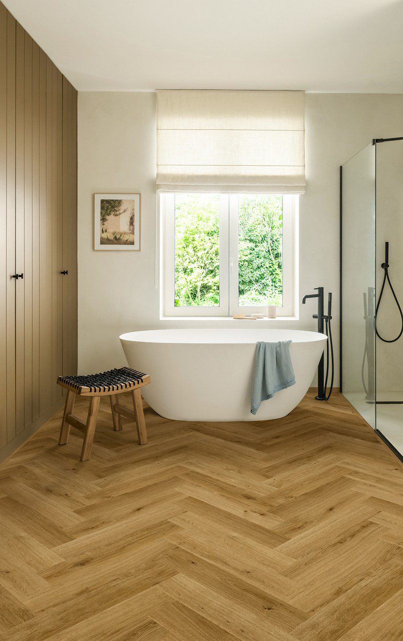 Herringbone laminate floor Quick-Step Impressive Design Cinnamon installed to bathroom floor. White separately standing bath.