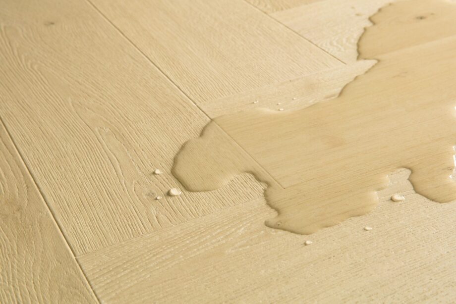 Kalanruoto laminaatti Quick Step Impressive Disain Ginger Oak, lämmin keskiruskea tammen sävy ja tasainen lajitelma, vesilätäkkö osoittamassa vedenkestävyyttä