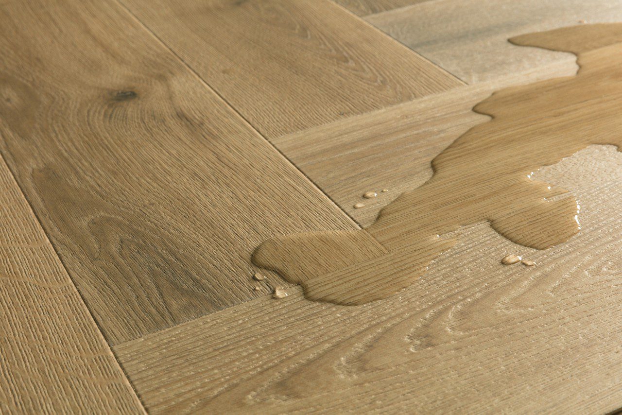 Klasaba laminaat Quick-Step Impressive Design Charred Oak tooni ja disaini kirjeldus. Laminaatparketil on veeloik näitamaks laminaatparketi veekindlust.