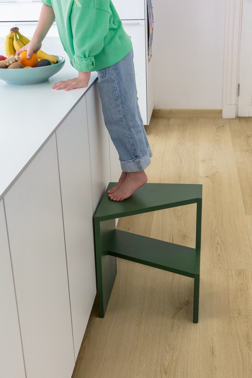 Klick Vinylboden Quick Step Bloom Botanic Beige in der Küche verlegt, ein Kind steht auf einem Stuhl und nimmt eine Orange aus einer Obstschale auf der Kücheninsel.