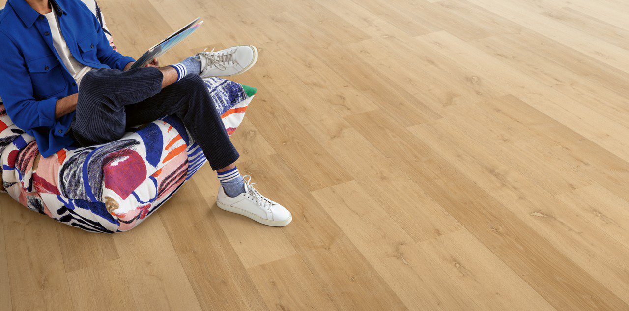 Klick Vinylboden Quick Step Bloom Elegant Oak Natural im Wohnzimmer verlegt, ein Mann sitzt in einem Sessel.