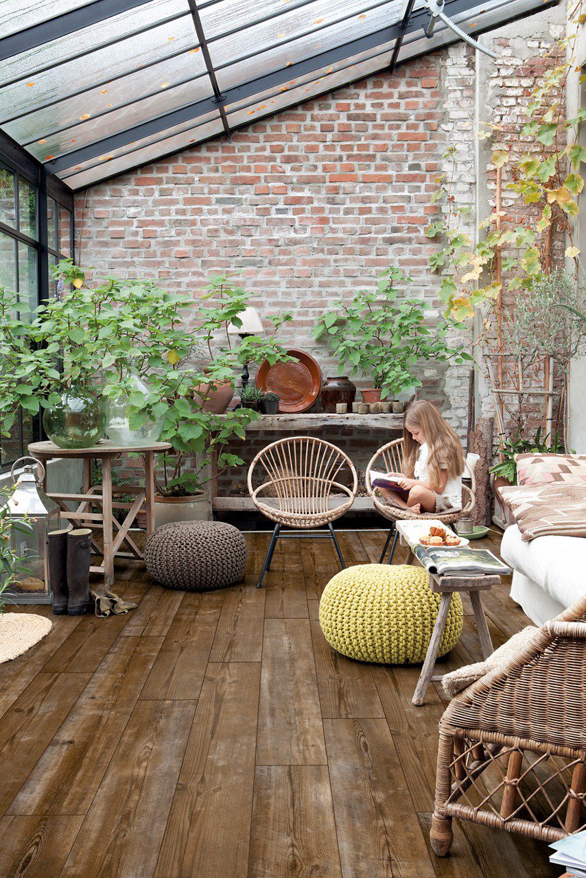 LVT parkett Quick-Step Bloom Sundown Pine paigaldatud talveaia põrandale. Potitaimed, trrassimööbel, laps istub toolil ja loeb raamatut.