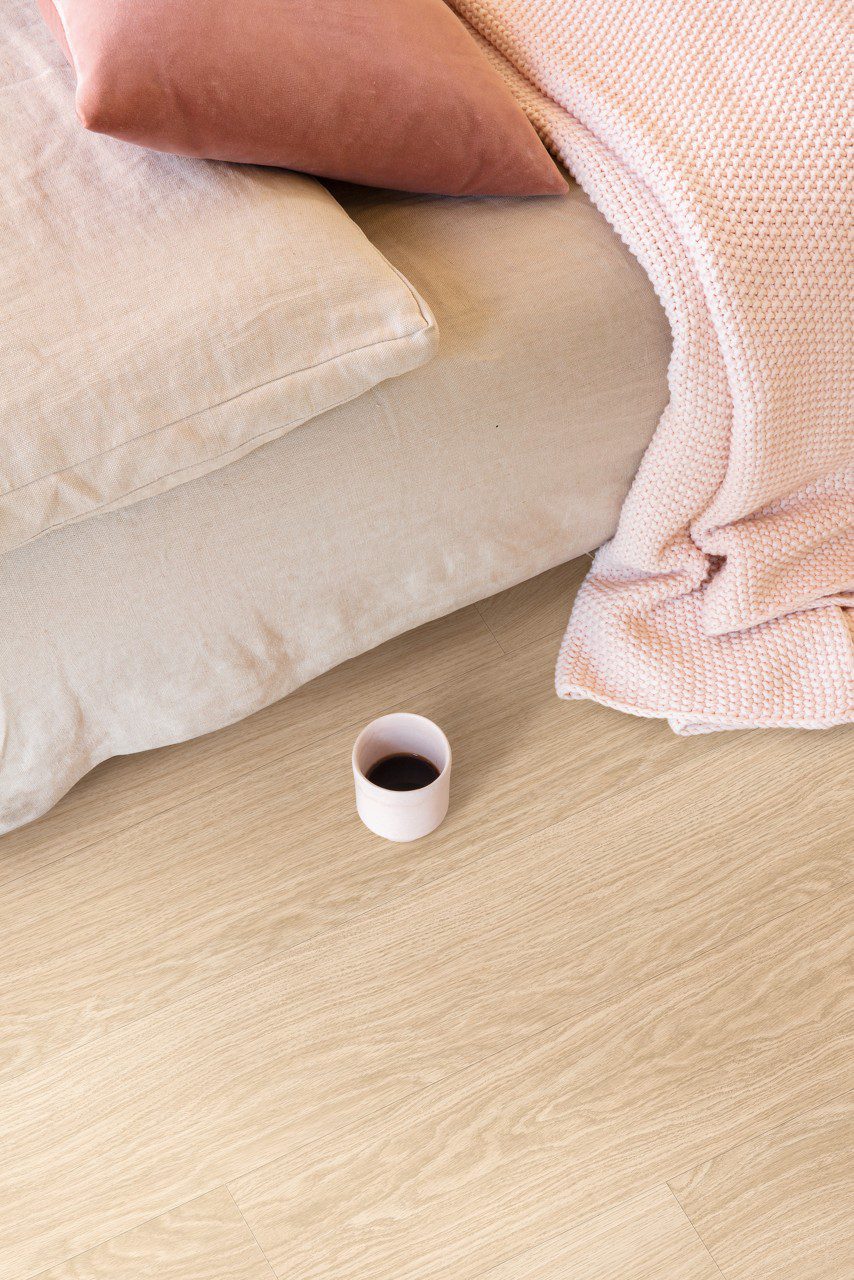 LVT põrandakate Quick-Step Bloom Pure Oak Blush paigaldatud magamistoa põrandale. voodi ja kohvitass põrandal