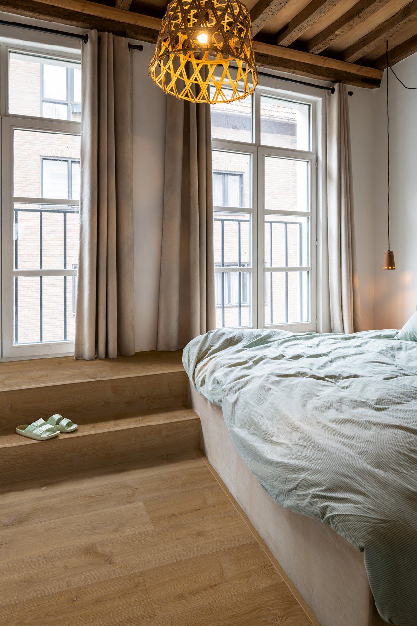 Rigid LVT flooring Quick-Step Bloom Elegant Fumed Oak installed on a bedroom floor. Big bed, Classical design widows from Ceiling to Floor.