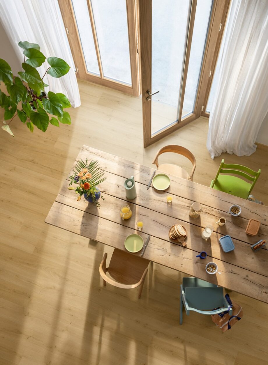 Rigid Vinylboden Quick Step Bloom Brushed Oak Honey im Esszimmer verlegt, Esstisch und Stühle, Blumen, Frühstück auf dem Tisch.