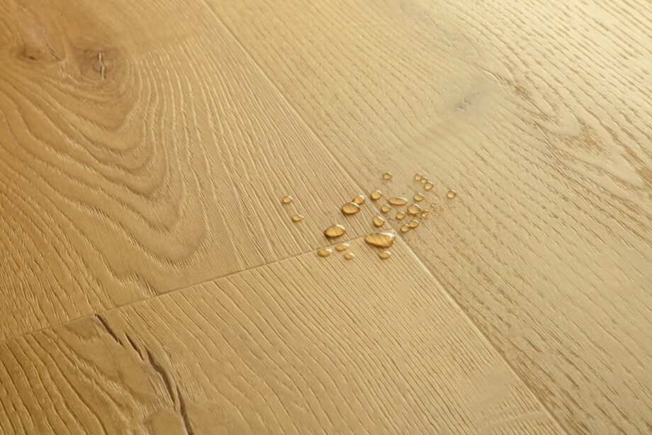 Vinüülparkett Quick-Step Bloom Brushed Oak Honey harjatud pind, soe tamme toon, veepiisad vinüülparketil näitamaks veekindlust.