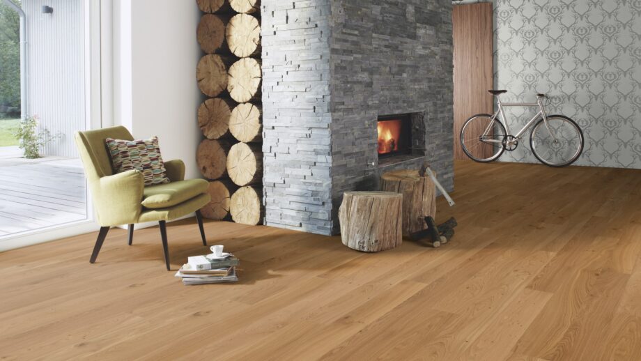 naturaalparkett-bauwerk-casapark-budget-cut-tamm-35-harjatud-matt-lakk Naturaalparkett Bauwerk Casapark Budget Cut harjatud matt lakk paigaldatud koridori ja elutoa põrandale. Suur kiviga kaetud kamin milles tuli. Roheline tugitool.