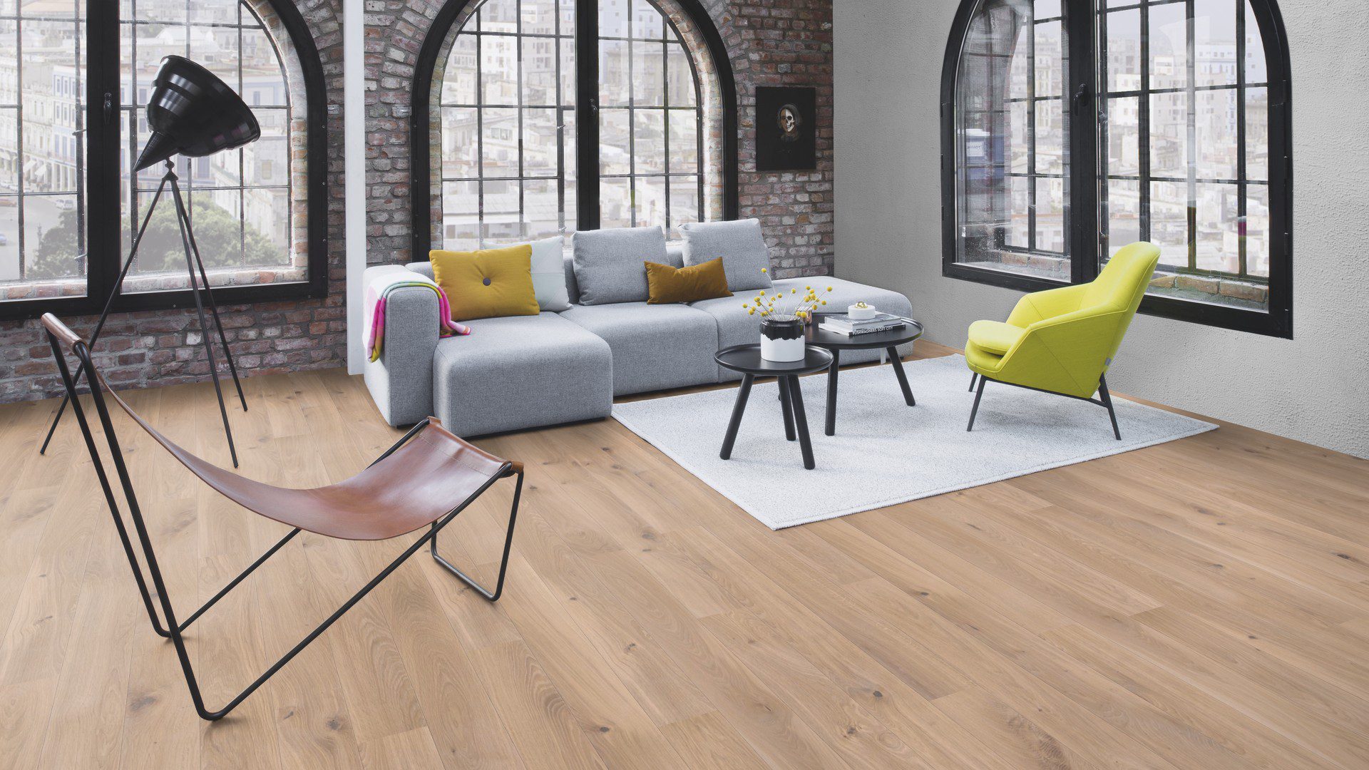 Parkett Bauwerk Boen Casapark Eiche 46 Farina, gebürstet und weiß geölt – verlegt auf dem Wohnzimmerboden; graues Sofa, leuchtend grüner Sessel und ein grauer Teppich mit zwei kleinen runden Couchtischen. Rustikale Sortierung mit lebendiger Maserung und Astanteilen.