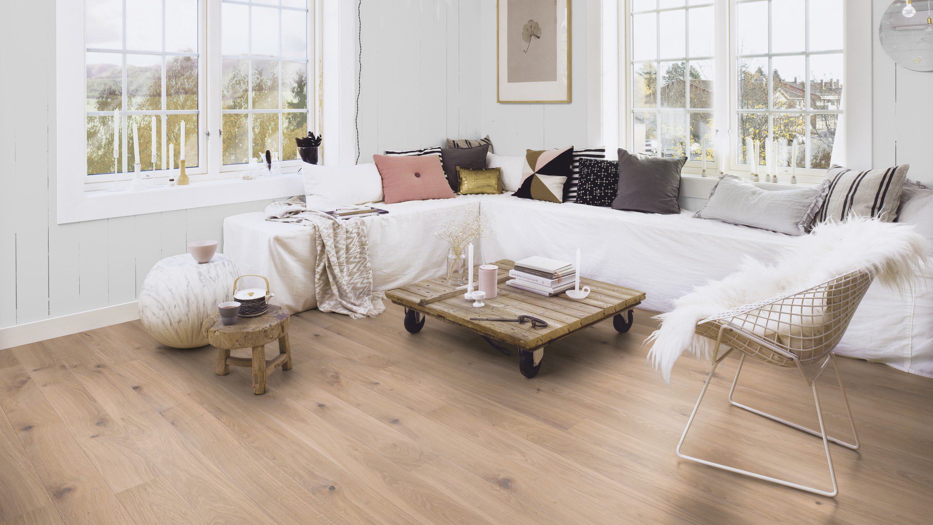 Tammeparkett Bauwerk Boen Casapark tamm 46 harjatud hele Farina õlivaha paigaldatud elutoa põrandale. Valge nurgadiivan erinevat tooni patjadega. Diivanilaud millel küünlad ja raamatud.