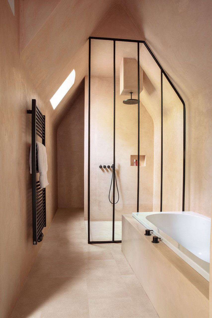 Кварц-винил Quick Step Oro Coral Rock уложен на пол в ванной комнате тёплый каменный дизайн в кораллово песочном оттенке естественная фактура и мягкие переходы цвета встроенная ванна чёрная душевая перегородка полотенцесушитель на стене и смесители