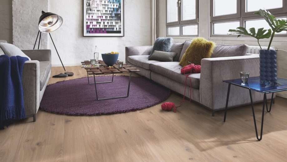 Laudparkett Bauwerk Casapark tamm 46 Crema harjatud ja heleda Bprotect lakiga viimistletud. Parkett on paigaldatud elutoa põrandale. Kaks diivanit ja disainer diivanilaud millel kauss kartulikrõpsudega, veepudel ja veeklaasid. Diivainilaua all on ümar tükivaip.