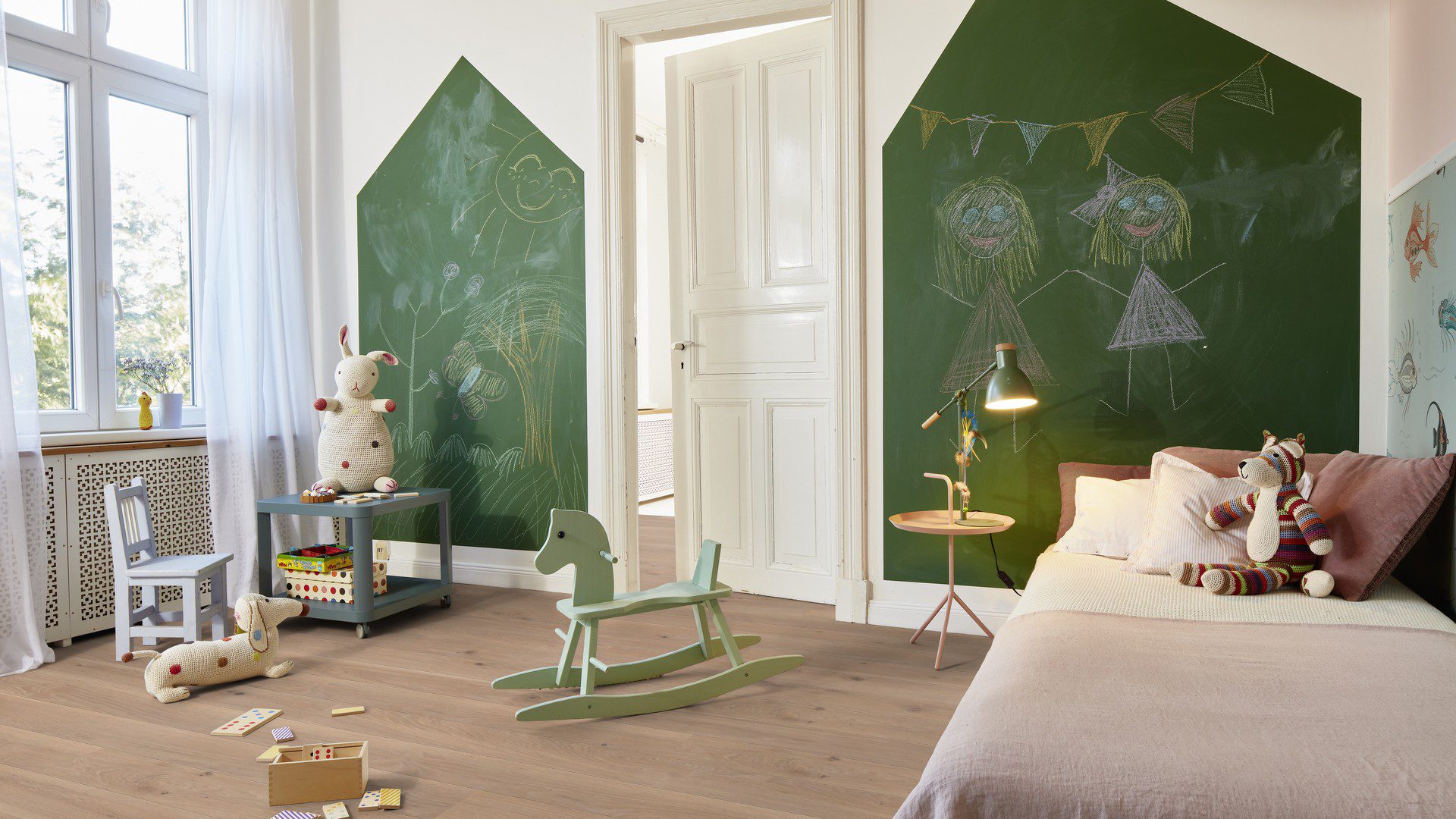 Tammeparkett Bauwerk Casapark tamm 35 Crema harjatud ja B-protect ultra matt lakiga viimistletud paigaldatud lastetoa põrandale. Voodi koos pehme mänguasjaga, kiiktool ja suured rohelised tahvlid seinal kriitidega joonistamiseks.