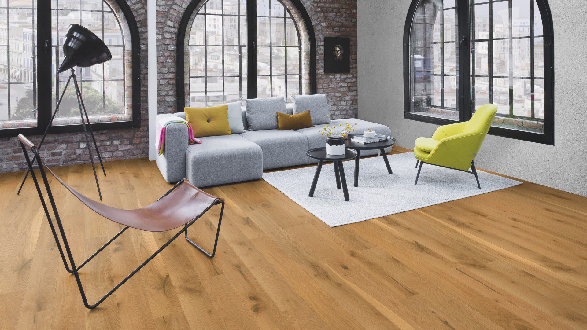 Tammiparketti Bauwerk Casapark Tammi 56 harjattu öljyvahattu asennettuna olohuoneen lattialle – harmaa sohva, keltainen nojatuoli ja pienet pyöreät sohvapöydät, joiden alla on harmaa tilkkumatto; luonnollinen tammen sävy, harjattu pinta ja elävä puukuvio.