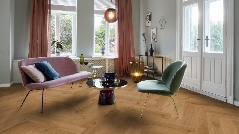 Helles, stilvolles Wohnzimmer mit Fischgrätparkett aus Eiche Mix (140 mm, geölt). Die Einrichtung kombiniert zartrosa Sofa, salbeigrünen Disainstuhl und einen modernen Couchtisch mit goldenen Akzenten. Große weiße Flügeltüren und Fenster bringen viel Tageslicht in den Raum. Warme Vorhänge, moderne Kunstobjekte und eine elegante Ambienteleuchte schaffen eine harmonische und einladende Atmosphäre. Kalasaba parkett Tamm Mix õlivahatatud 140mm – vaade 9