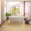 Laminat Fischgrät Quick Step Impressive Disain Ginger Oak, verlegt im Badezimmerboden, freistehende weiße Badewanne, mit blauer Mosaikfliese verkleideter Sockel und rote Fensterrahmen
