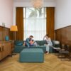 vinyl-fischgrät-quick-step-ciro-botanic-smoked-oak Vinyl Fischgrat Quick Step Ciro Botanic Smoked Oak, verlegt auf dem Wohnzimmerboden, ein Mann, eine Frau und ihre Tochter kuscheln auf einem blauen Sofa.