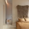 klickvinyl-quick-step-bloom-sea-breeze-oak-light Klickvinyl Quick Step Bloom Sea Breeze Oak Light im Schlafzimmer verlegt, sehr heller Eicheton und Dielendesign, Bett mit schöner hellbrauner Bettwäsche, im Hintergrund ein Badezimmer mit freistehender, eckiger Disain-Badewanne.