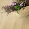 LVT floor Quick-Step Bloom Botanic Beige installed on a floor. On the floor is laying open bag with many different beautiful pink flowers.