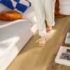 LVT flooring Quick-Step Bloom brushed oak honey installed on a livingroom floor. Woman walking on the floor, sofa and sofa table.