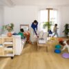 LVT parkett Quick-Step Bloom brushed oak honey paigaldatud elutoa põrandale. Ema koos kahe lapsega, koer, diican, lilled, riiul, telekalaud.