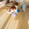 LVT põrandakate Quick Step Bloom brushed oak honey paigaldatud elutoa põrandale. Tüdruk, koer, telekalaud, diivan.
