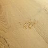 Vinüülparkett Quick-Step Bloom Brushed Oak Honey harjatud pind, soe tamme toon, veepiisad vinüülparketil näitamaks veekindlust.