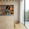 Vinyylilattia Quick Step Bloom Botanic Beige asennettuna keittiön lattialle, nainen kohentaa keittiösaarella olevaa ruukkukasvia, vaalea luonnonbeige sävy ja lankkudesign.