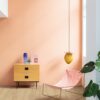Виниловый ламинат Quick Step Bloom Botanic Beige уложен на полу в коридоре, розовый стул, комод и лампа, женщина моет пол шваброй.