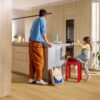 Виниловый ламинат Quick Step Bloom Brushed Oak Honey уложен на полу на кухне, отец и дочь у кухонного острова, рядом собака.