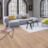 Parkett Bauwerk Boen Casapark Eiche 46 Farina, gebürstet und weiß geölt – verlegt auf dem Wohnzimmerboden; graues Sofa, leuchtend grüner Sessel und ein grauer Teppich mit zwei kleinen runden Couchtischen. Rustikale Sortierung mit lebendiger Maserung und Astanteilen.