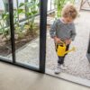 LVT flooring tiles Quick-Step Illume Oyster concrete with light grey color installed in hallway and kid is coming inside from summer garden.