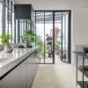 Vinyl tiles Quick-Step Illume Oyster concete installed on a kitchen floor. Kitchen furniture, opened door to summer garden and father and son are watering plants there.