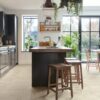 Vinyl tiles Quick-Step Illume Pebble concrete installed on a kitchen floor. Kitchen furniture with an island, rustical style stools next to it.