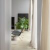 Vinylboden in Betonoptik Quick-Step Illume Pebble Concrete, verlegt auf dem Wohnzimmerboden – schwarze Lederstühle, luftige Vorhänge und eine Zimmerpflanze.