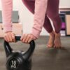 vinylboden-stein-quick-step-oro-oxidized-rock Frau macht Übungen mit einer 10-kg-Kettlebell in einem eingerichteten Home-Gym auf dem neu verlegten Vinylboden in Steinoptik Quick-Step Oro Oxidized Rock.