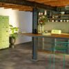 vinylboden-steinoptik-quick-step-oro-oxidized-rock Vinylboden in Steinoptik Quick Step Oro Oxidized Rock in einer rustikalen Küche verlegt rostig kupferbrauner Farbton mit lebendiger Struktur industrieller Steinlook metallische alte Träger und Holzbalken an der Decke alter Küchenschrank Regale Esstisch und Stuhl
