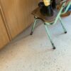 Кварц-винил Quick-Step Illume Pebble Concrete уложен на полу кухни — ребёнок стоит на старом стиле стуле, рядом стоит отец; светлый бетонный оттенок и спокойный бетонный дизайн.
