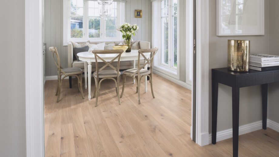 Naturaalparkett Bauwerk Casapark tamm 46 Crema harjatud ja heleda ultra mattlakiga viimistletud. Paigaldatud klassikalises stiilis söögitoa põrandale. Klassikaline valge söögilaud millel valged lilled. Toolid ja diivan söögilaua ümber.
